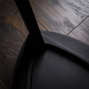 Crna drvena hoklica sa sedalom u obliku Reuleaux trougla i tri blago zakošene noge, fotografisana na tamnom drvenom podu uz sivi betonski zid u pozadini.