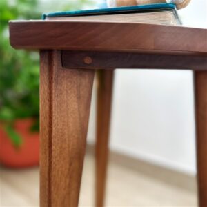 Kado ručno rađen drveni stočić od oraha sa zaobljenim gornjim delom i drvenim spojevima, prikazan u modernom enterijeru